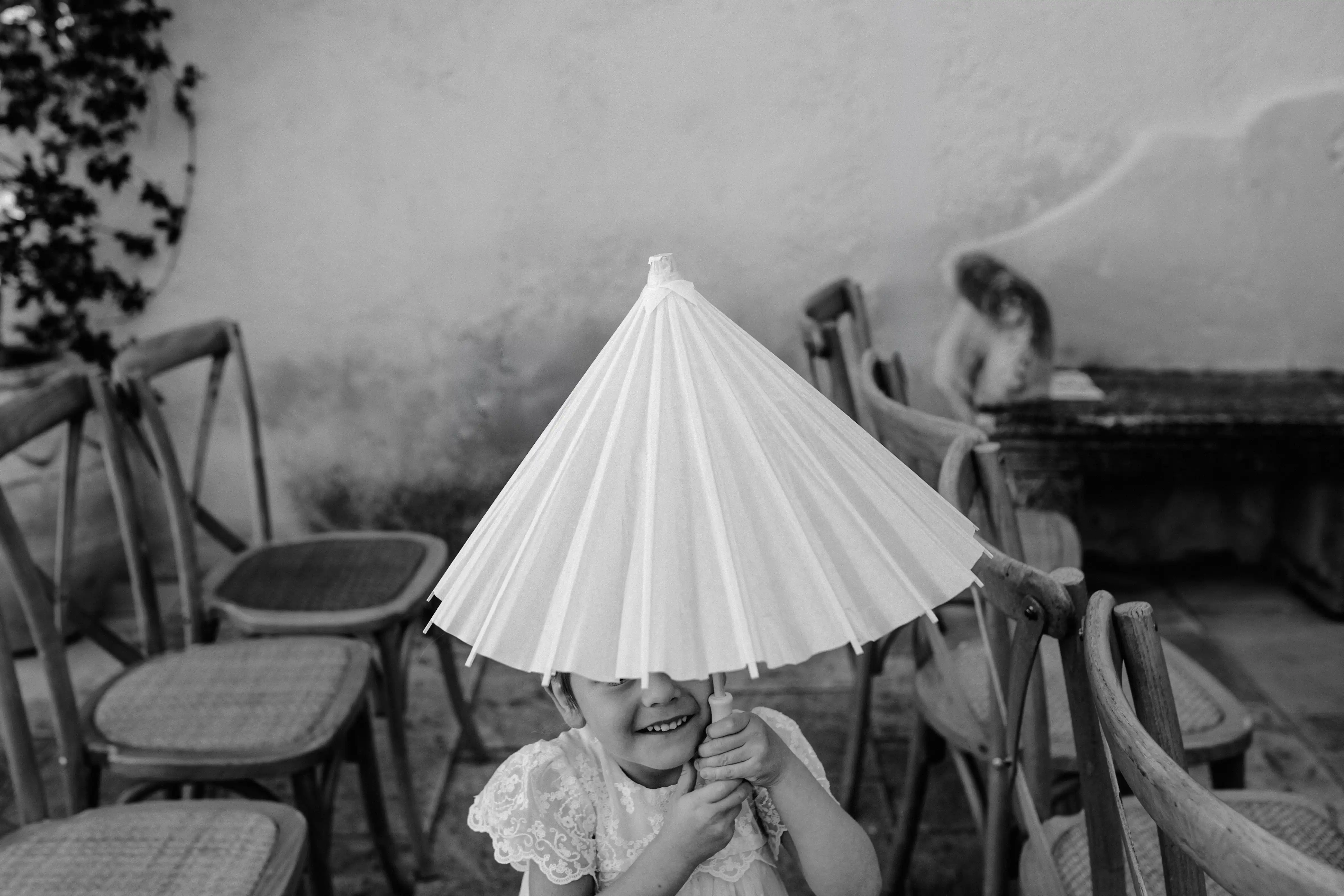 Little flower girl hiding under a paper parasol during a destination wedding in Sicily.